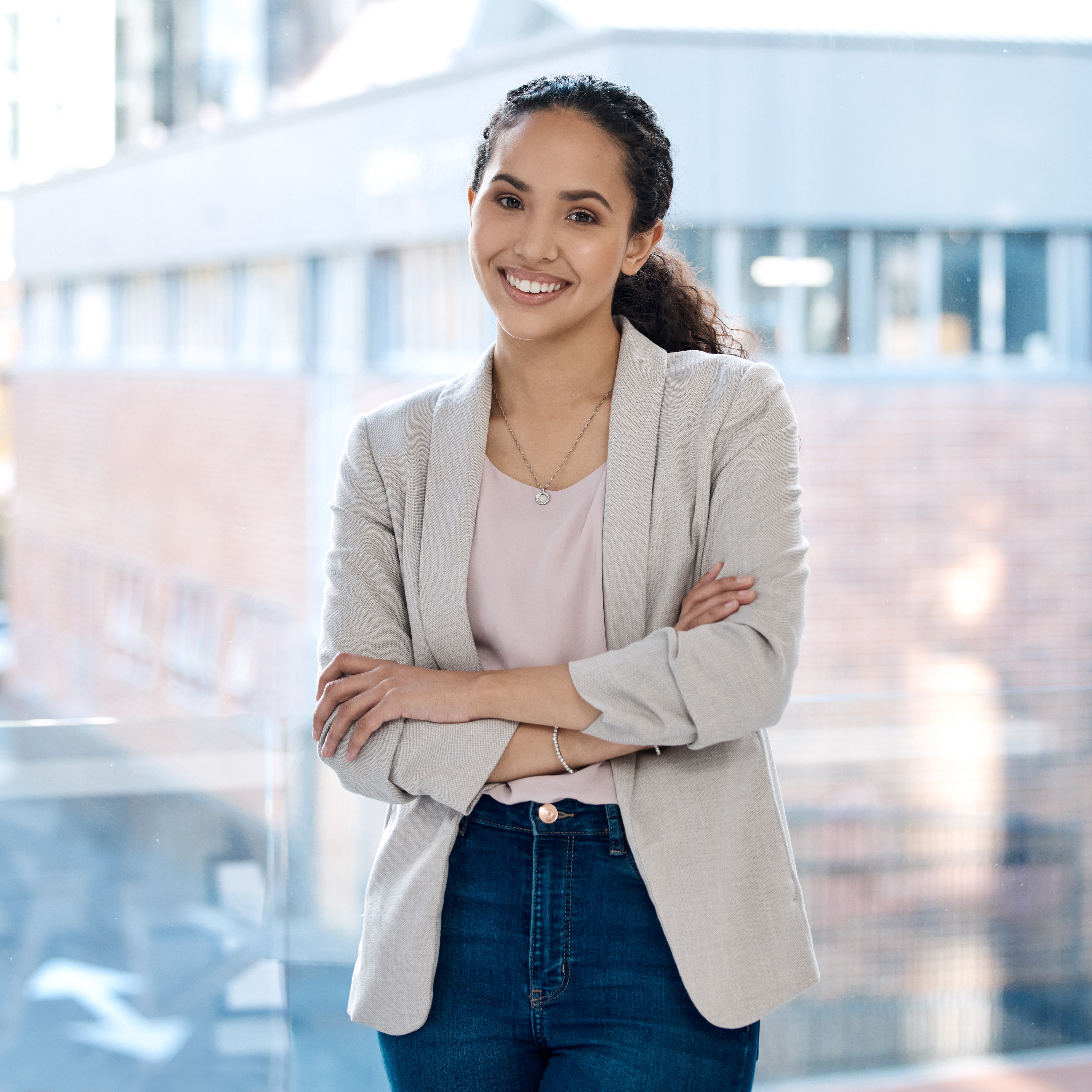 Portrait of a happy mixed race businesswoman standing with her arms crossed alone in her office. On